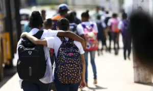 Adolescentes de costas se abraçando com mochila nas costas e indo pra escola